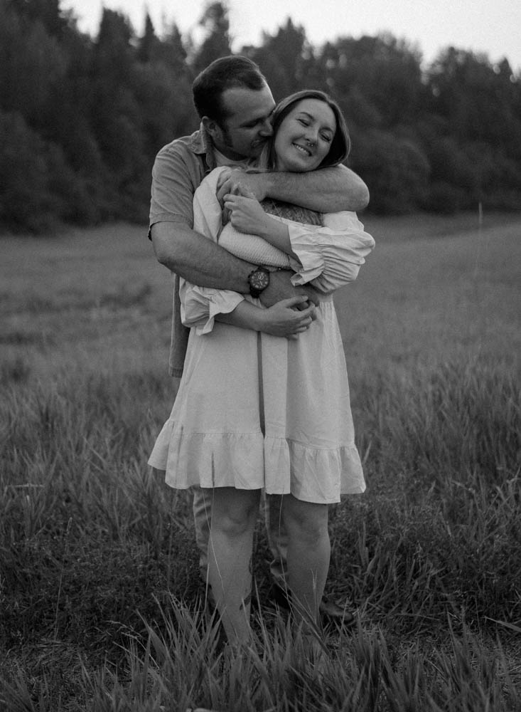couple standing in a field hugging and kissing during sunset