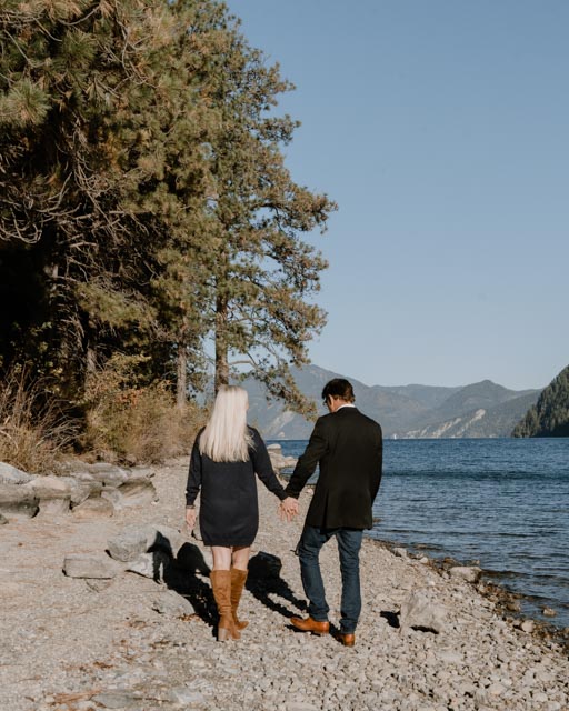 couple walking along the lake on a rocky beach in the Fall on a sunny day.