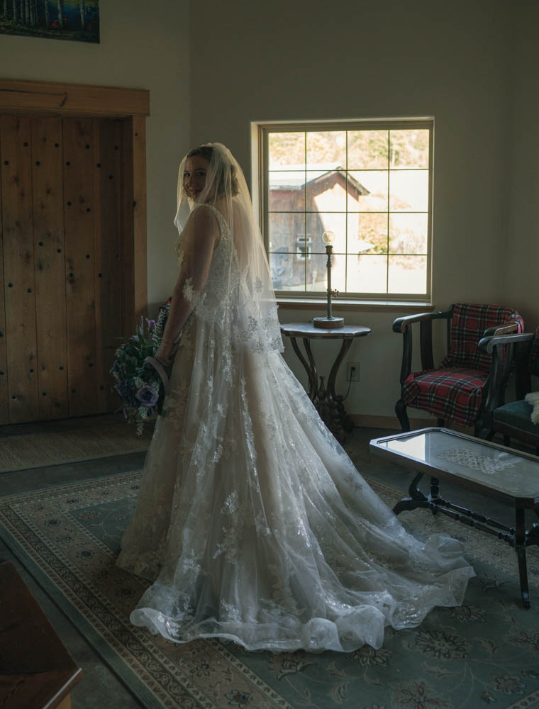 bride in her dress as she stands looking over her shoulder and holding her bouquet. 
