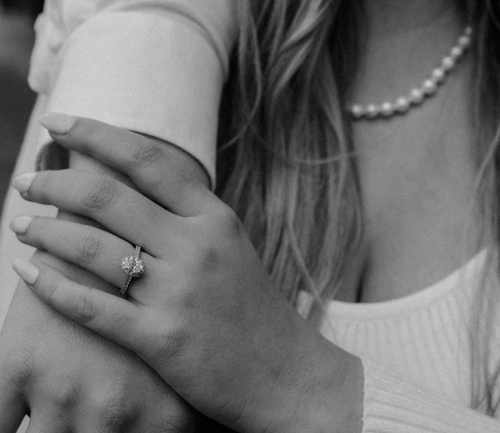 detail of an engagement ring on the woman's finger as she holds her fiances hand.