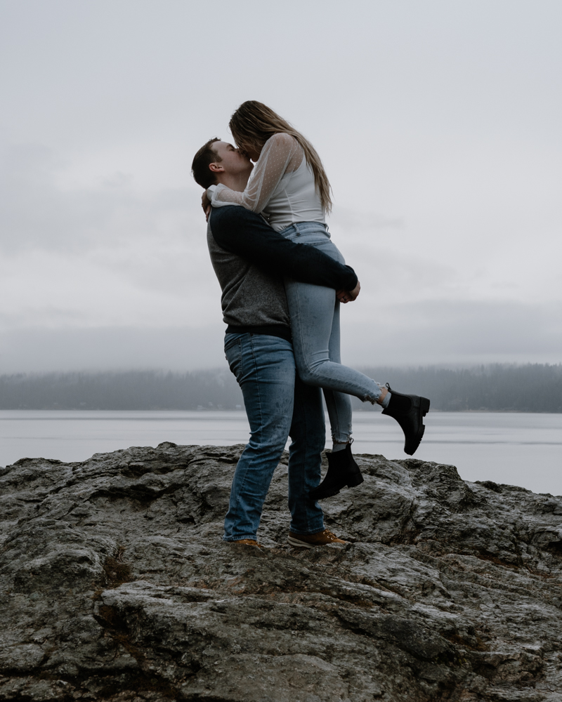 man holding up his fiance as they kiss overlooking Lake Coeur d' Alene.