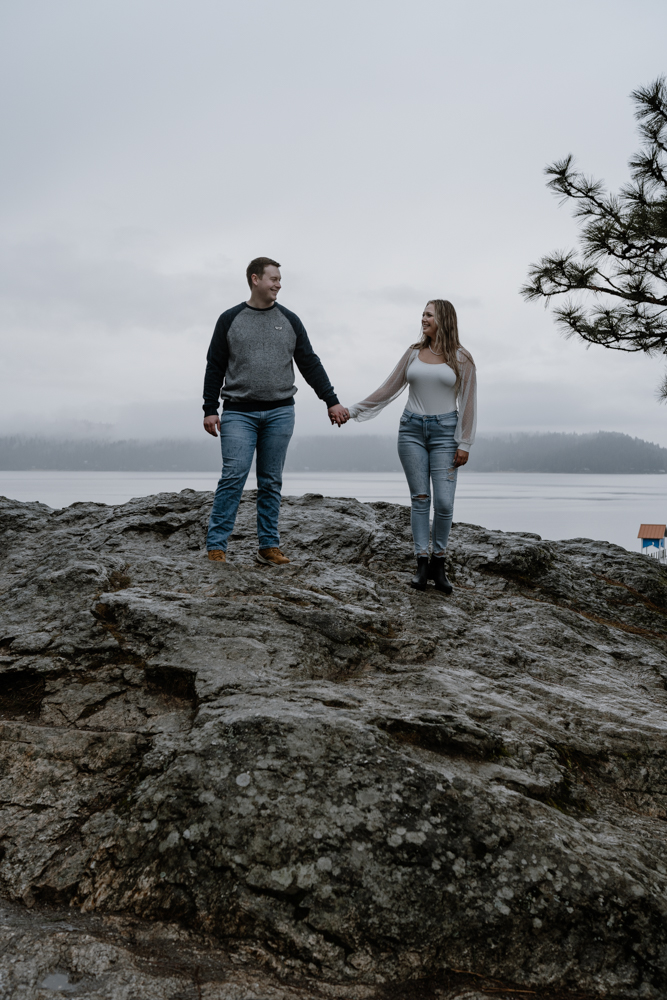 couple standing on a large rock holding hands and looking at each other.