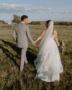 bride and groom holding hands as they walk in the field. 