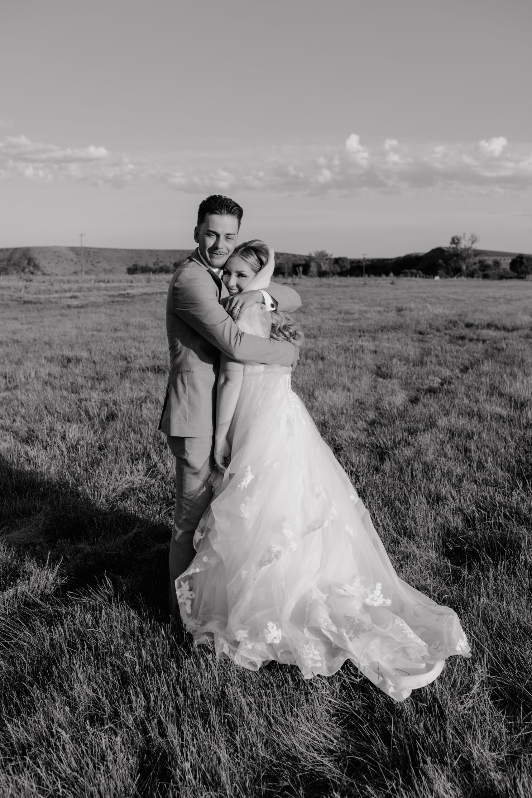bride and groom hugging and smiling in a field.