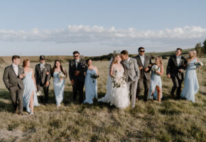 bride and groom kissing while walking in a field with the bridal party.