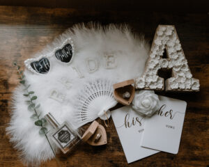 lay flat of bride and groom details such as rings, vow books, custom heart shaped sunglasses a feathery fan and groom's cologne.