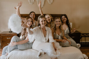 Bride and bridesmaids gathered up on the bed cheering for the bride.