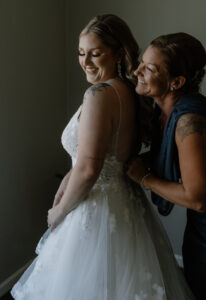 mother and bride smiling as mother of the bride button's up bride's dress.