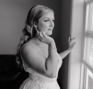 bride standing at the window looking out and touching her earring.