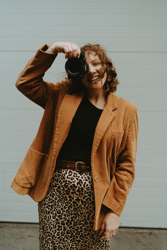 engagement photographer holding a camera up to her face as she smiles