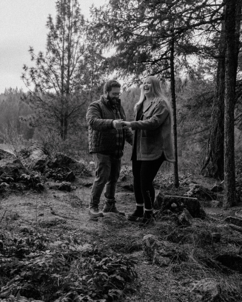 Couple laughing after husband helps his wife from atop a tree stump.  