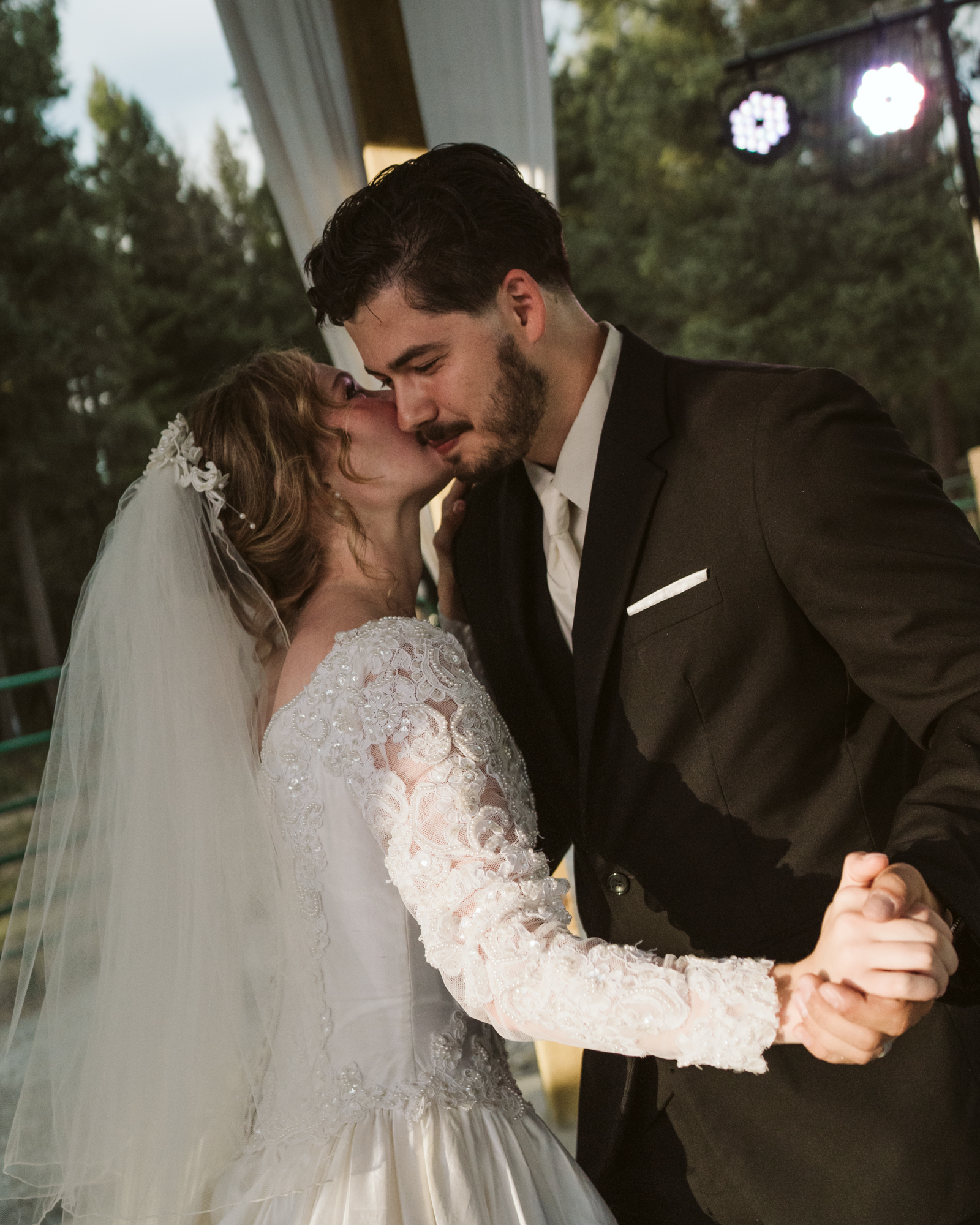 bride kissing the groom on his cheek as they hold hands while dancing their first dance as husband and wife.